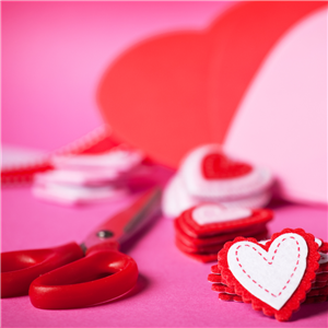A pair of red scissors sits next to a stack of red felt hearts
