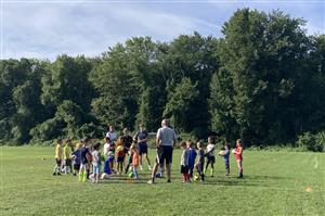 4-8 year olds surround Coach Jim in a soccer field 