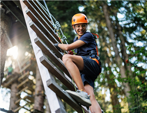 teen boy climbing up ladder with a climbing harness and helmet on