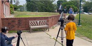 Two students use film cameras while 3 students act out a scene