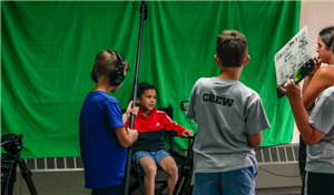 a group of 4 kids filming a scene in front of a green screen